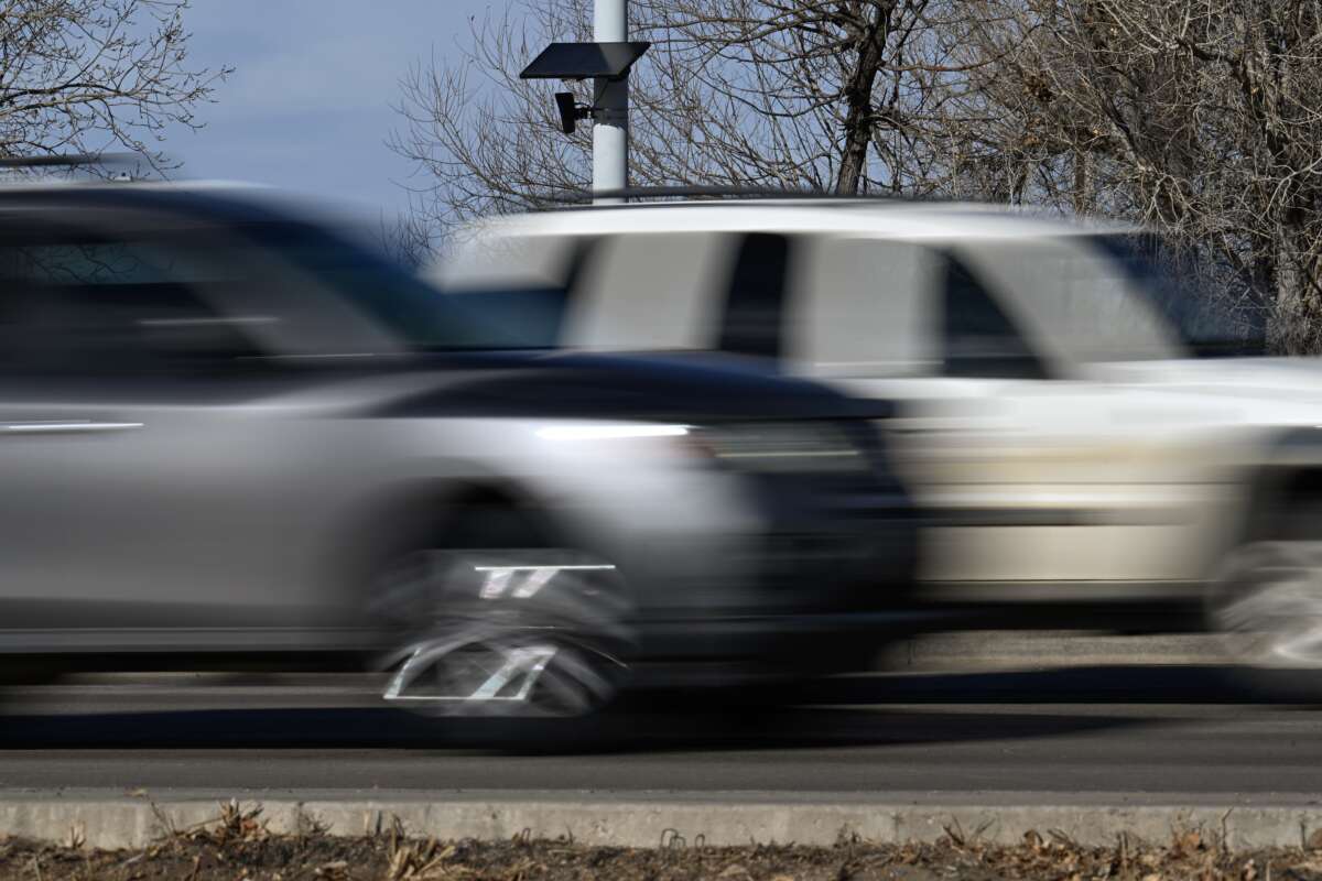 A Flock Safety license plate recognition camera is seen on a street light post as vehicles pass by in Longmont, Colorado, on December 10, 2025.