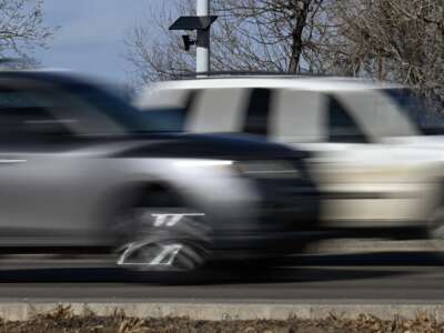 A Flock Safety license plate recognition camera is seen on a street light post as vehicles pass by in Longmont, Colorado, on December 10, 2025.