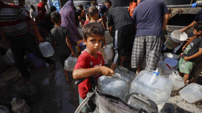 A Palestinian child stands next to a wheelchair loaded with water containers near a water distribution truck in Al-Shati refugee camp, west of Gaza City, Gaza Strip, on July 4, 2026.