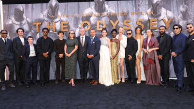 The cast of The Odyssey stands in front of a banner.