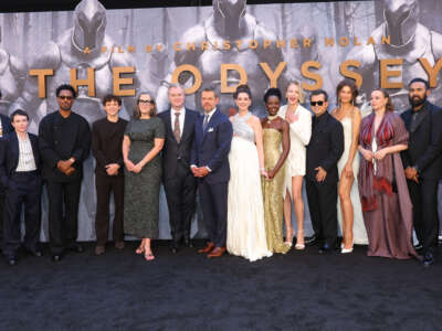 The cast of The Odyssey stands in front of a banner.