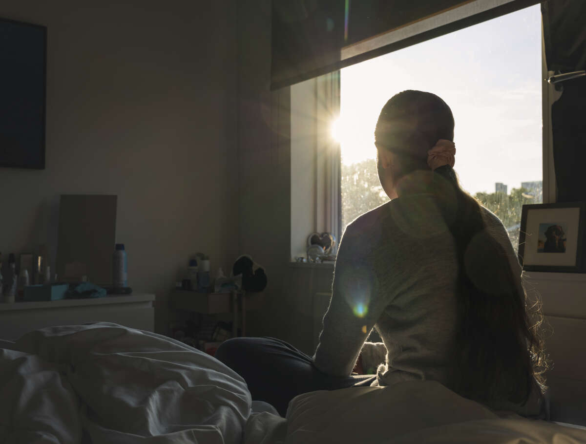 Shot of a teenage girl looking out of her bedroom window as the late sun streams in.