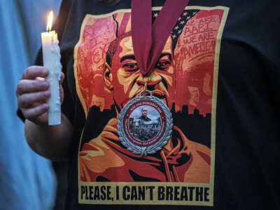 A person holds a candle while wearing a George Floyd t-shirt and a "Rise and Remember 2025" medallion during a vigil at George Floyd Square in Minneapolis, Minnesota, on May 25, 2025, the fifth anniversary of Floyd's death.