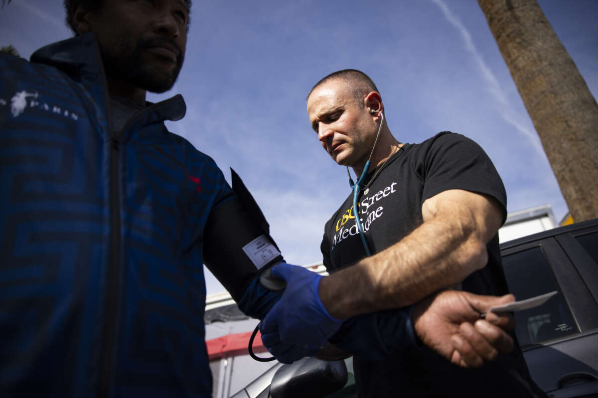 Charles Wilkerson III, 43, left, gets his blood pressure taken by USC Director of Street Medicine Brett Feldman, right, at the intersection of James M. Wood Boulevard and Beacon Avenue on Monday, February 23, 2026 in Los Angeles, California. Brett Feldman and the USC Street Medicine team provide medical care to the unhoused community in Los Angeles.