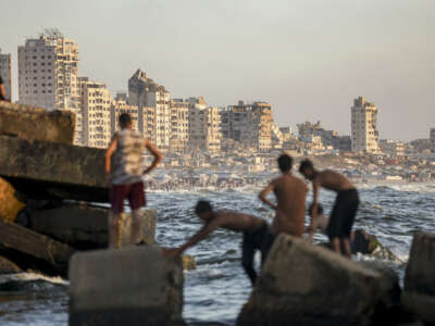 Palestinian youths stand and swim along a rocky breakwater on the Mediterranean coast in Gaza City, on July 4, 2026.