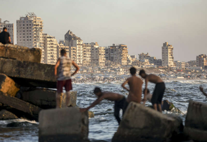 Palestinian youths stand and swim along a rocky breakwater on the Mediterranean coast in Gaza City, on July 4, 2026.