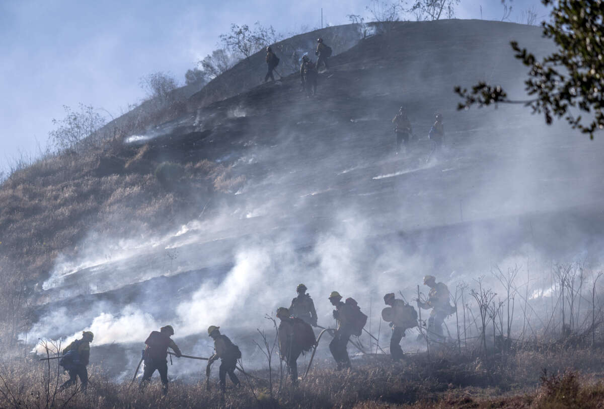 Orange County Fire Authority firefighters work to extinguish flames and embers on a dry, grassy hillside at Narrow Canyon Road and Acaster Way in Ladera Ranch, California, as they battle the Narrow fire on July 7, 2026.