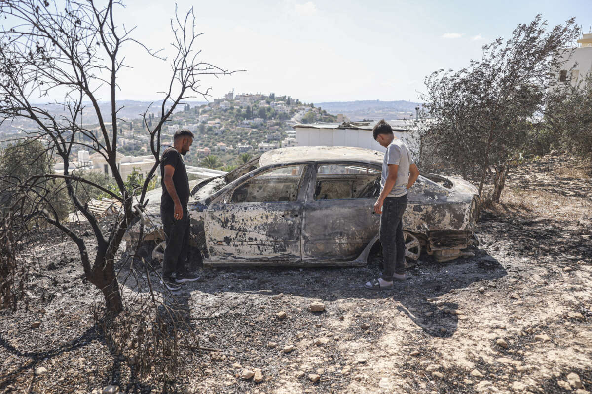 Two Palestinian men inspect a burned vehicle surrounded by scorched trees in Far'ata, east of Qalqilya in the occupied West Bank, on July 24, 2026, after Israeli settlers attacked the village injuring eight Palestinians with live ammunition and setting residents' property on fire.