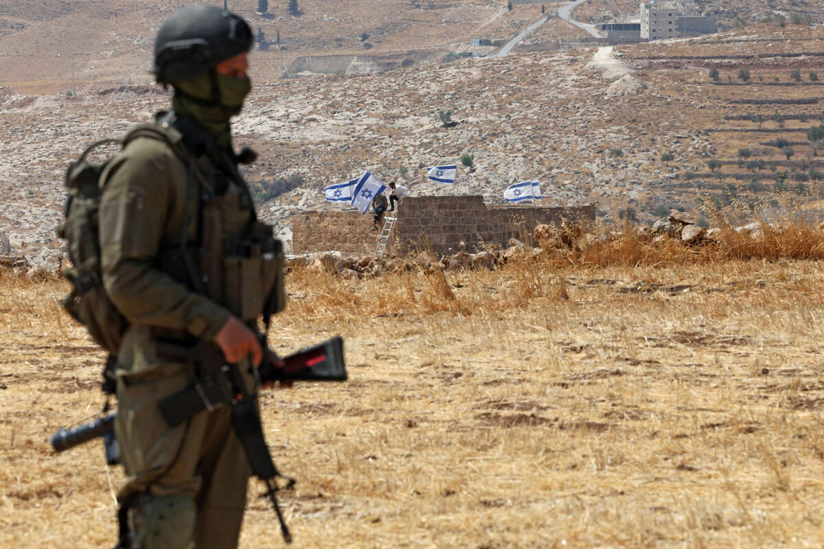 An Israeli soldier stands against the backdrop of a house seized by Israeli settlers in Beit Sahur, south of Bethlehem, in the occupied West Bank, on August 14, 2026.