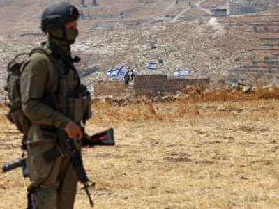An Israeli soldier stands against the backdrop of a house seized by Israeli settlers in Beit Sahur, south of Bethlehem, in the occupied West Bank, on August 14, 2026.
