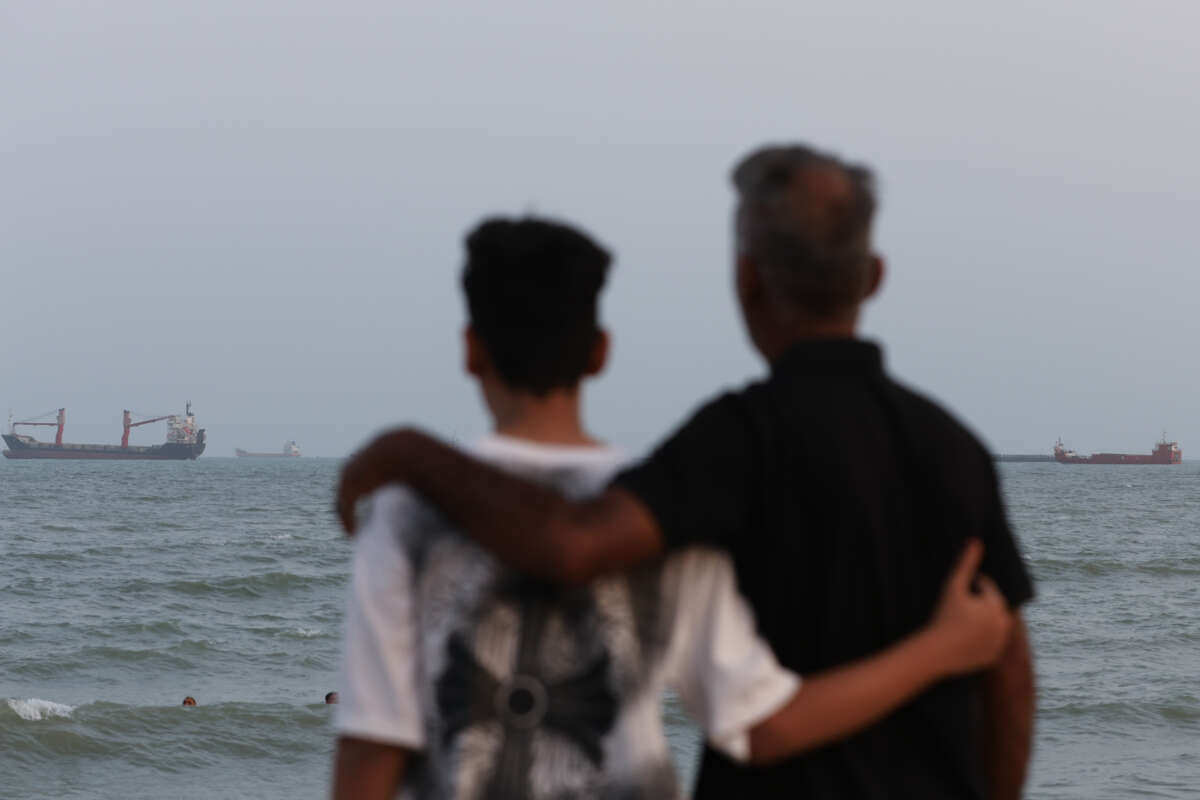 Two people embrace on the shoreline as ships are seen anchored in the Strait of Hormuz on August 10, 2026, off the coast of Bandar Abbas, Iran.