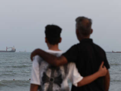 Two people embrace on the shoreline as ships are seen anchored in the Strait of Hormuz on August 10, 2026, off the coast of Bandar Abbas, Iran.