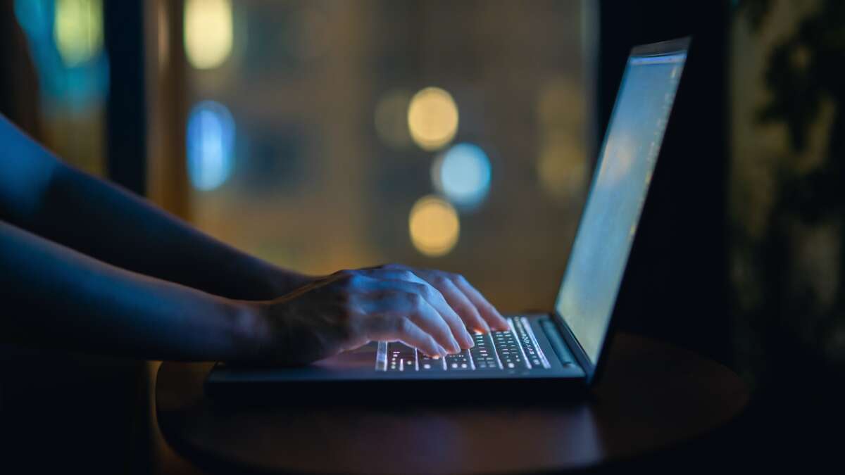 Cropped shot of woman's hand typing on computer keyboard in the dark, working late on laptop at home