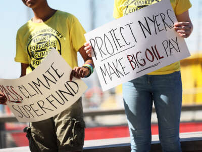 People hold signs during a press conference on the Climate Change Superfund Act at Pier 17 on May 26, 2023, in New York City.
