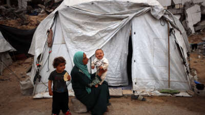 A Palestinian mother plays with her child as she sits in front of her tent in a displacement camp in Gaza City, on May 12, 2025.