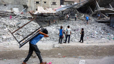 A boy walks carrying a table on his back past salvage workers scrapping the rubble of a building that was destroyed during Israel's assault on Gaza, to use the recycled remains in the future, in Gaza City, on August 16, 2026.
