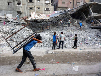 A boy walks carrying a table on his back past salvage workers scrapping the rubble of a building that was destroyed during Israel's assault on Gaza, to use the recycled remains in the future, in Gaza City, on August 16, 2026.