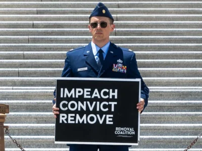 Air Force Major Jason Watson holds a sign reading "IMPEACH, CONVICT, REMOVE" on July 1, 2026, on the steps of the US Capitol in Washington, DC.
