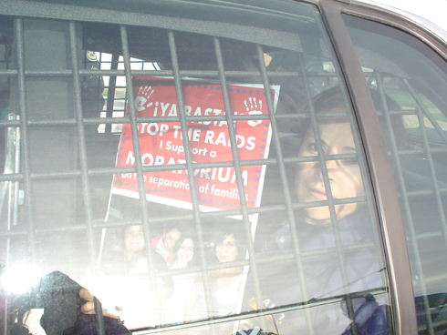 A labor leader waits in a police car after being arrested during the peaceful demonstration, holding a sign calling to stop the raids.