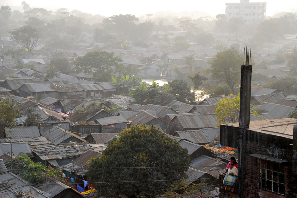Residents of a brick apartment building look out over the vast Bhashantek slum in Dhaka, Bangladesh.