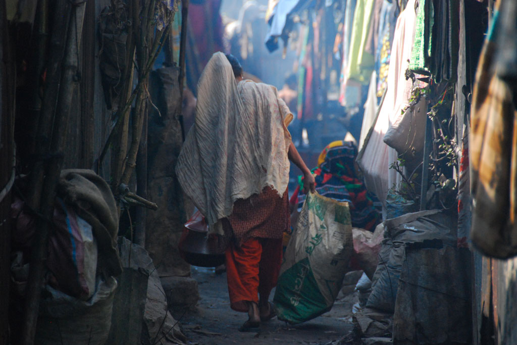 A heavily-laden woman carries water from a communal tap down a cramped side street in the Kallyanpur slum in Dhaka, Bangladesh.