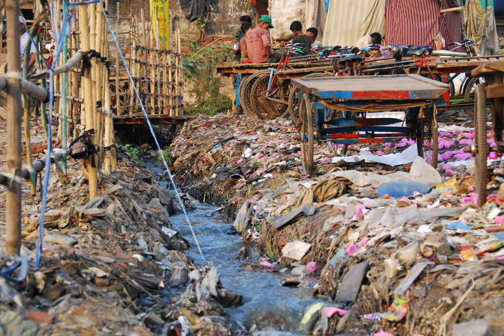 Raw sewage drains from a slum neighborhood directly onto the trash-strewn banks of the Buriganga River in Dhaka, Bangladesh.