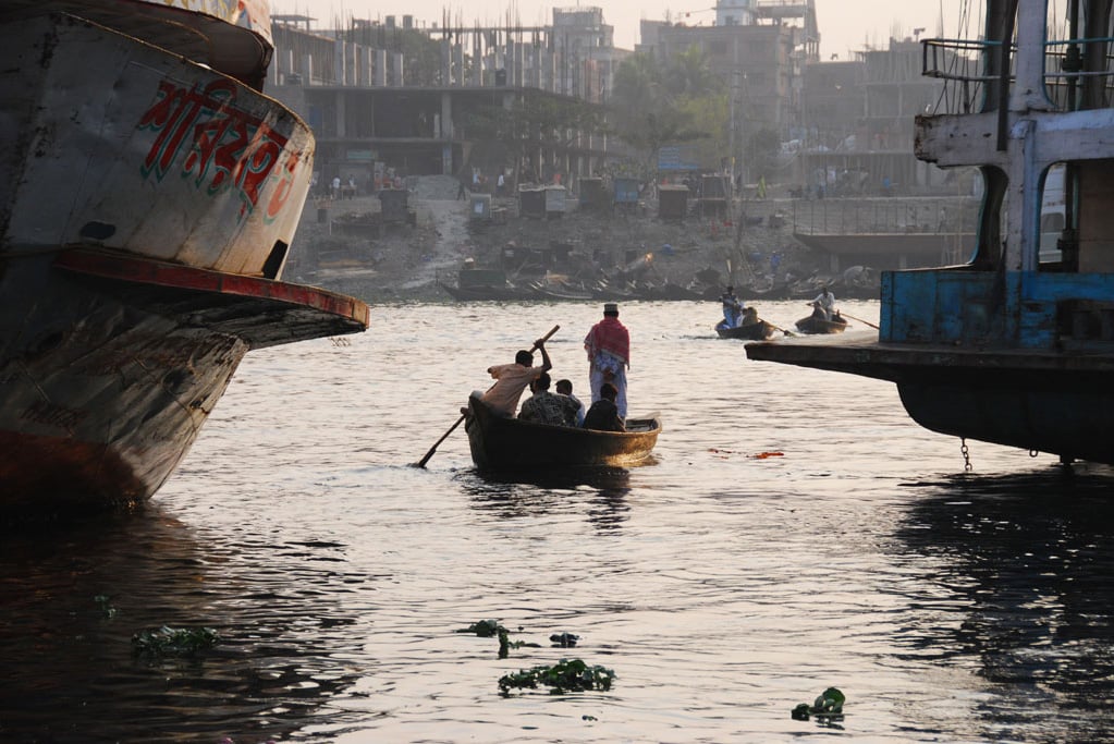 A small hand-powered water taxi threads its way between two huge paddle-wheel passenger vessels on the Buriganga River in Dhaka, Bangladesh.