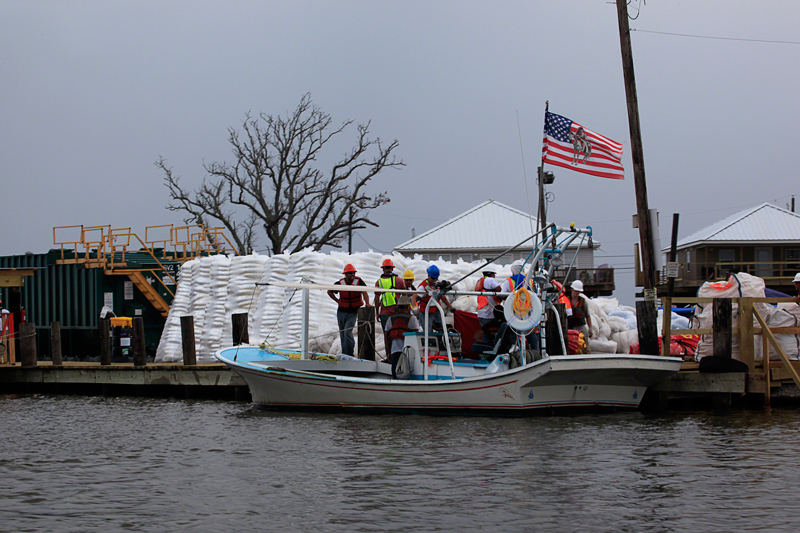 In the front of the Marina another US flag stands above more piles of  boom. Erika later finds, upon closer inspection of the photo, it has an  indigenous man atop a horse painted on the flag. Photo by Erika Blumenfeld.