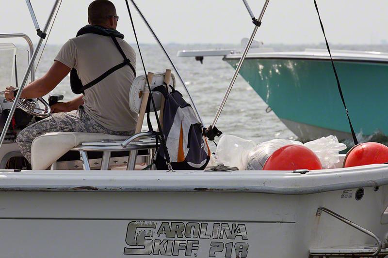 The boat is accompanied by an unmarked Carolina Skiff, driven by a man wearing desert camouflage pants and a tan shirt.