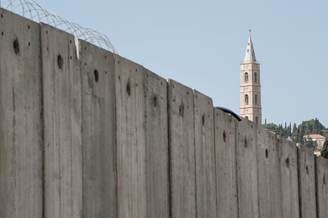 The belltower of the Russian Orthodox Church of the Ascension rises above the  Israeli separation wall that divides Palestinian neighborhoods on the Mount of Olives in East Jerusalem. (Photo: Courtesy of Ryan Beiler)