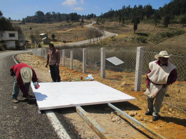 Candelaria residents paint over graffiti to fix up a roadside sign proclaiming their opposition to the highway project. (Photo: WNV / Sandra Cuffe)