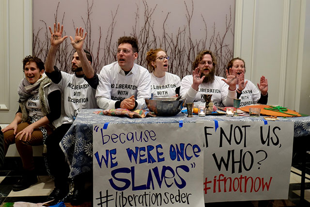 Six IfNotNow members chained to a ritual seder table inside the lobby of AIPAC. (Photo: Sam Boaz)