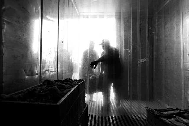 Two men bring crates of fish into an industrial refrigerator for storage. (Photo: Michael Stein)