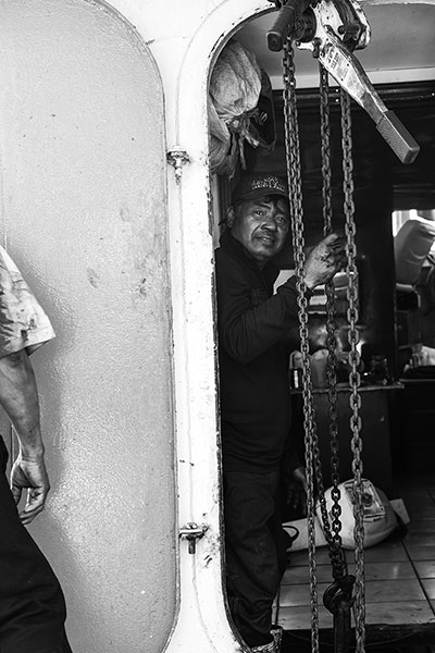 The crew of a shrimping vessel lowers a new engine into the hull of their ship. (Photo: Michael Stein)