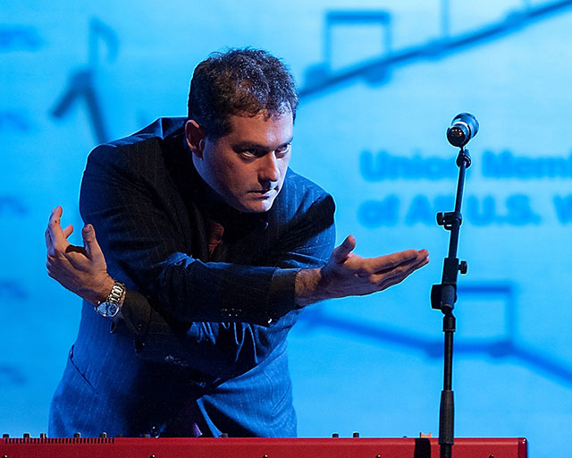 Bogad as the Economusician, performing economic data as music, his arms twisted by the piano score of Inequality. Helsinki, 2012.