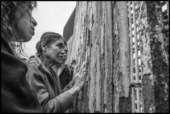 In Playas de Tijuana, on the Mexican side of the border wall between Mexico and the US, Catelina Cespedes and Carlos Alcaide greet Florita Galvez, who is on the US side. The family came from Santa Monica Cohetzala in Puebla to meet at the wall. (Photo: David Bacon)