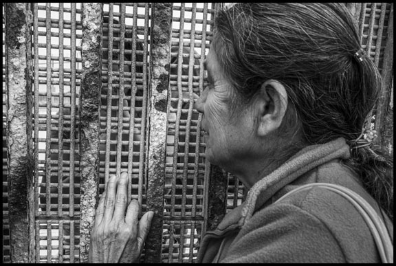 On the Mexican side of the border wall Catelina Cespedes sticks her finger through a hole in the mesh so that she can touch the finger of her daughter, Florita Galvez, on the other side. (Photo: David Bacon)