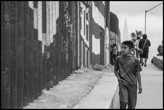 A boy walks past the Mexican side of the border wall between Mexico and the US. (Photo: David Bacon)