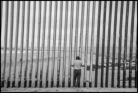 A man looks through the bars of the border wall into the US. (Photo: David Bacon)