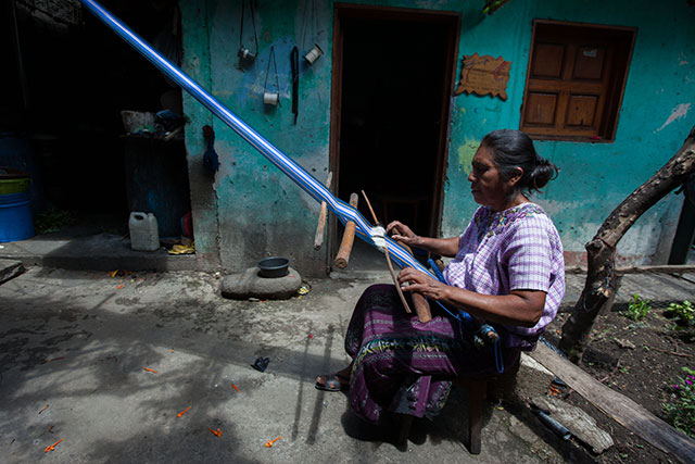 A member of the 13 B'atz' weavers collective sits in the garden of her house in Santiago Atitla and using a backstrap loom to weave one of the famous pieces. (Photo: Jeff Abbott)