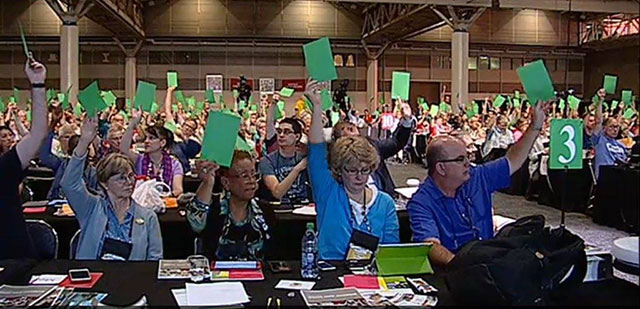 Participants in the 14th triennial Churchwide Assembly of the Evangelical Lutheran Church of America (ELCA) raise green cards in the air to signal their support for a measure to steer their church away from investing in the Israeli occupation of Palestine. (Photo: ELCA)