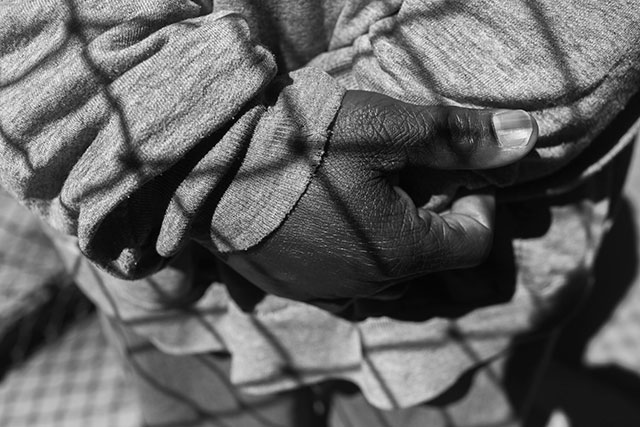 8. An outdoor chain link fence casts a shadow across Emmanuel Steward's hands. (Photo: Annie Flanagan)