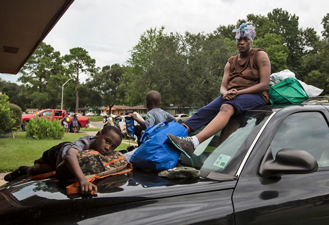 Adrianna Norwood and her two sons sit on her destroyed car in front of the flooded home she rents, with nowhere to go. The main shelters turned them away because they were full, so they slept in a different church every night until her son who has epilepsy had two convulsions. Only then was the family taken in at the Medical Special Needs Shelter at the LSU where her son could get medical help. (Photo: Julie Dermansky)