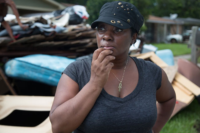 Roxanna Johnson in front of her flooded home in East Fariline, a subdivision in Baton Rouge, surveying her block. (Photo: Julie Dermansky)