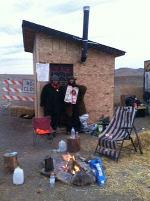 Two guards at a security hut are part of the intricate organization of the Water Protectors' camp. Their job is to guarantee peace and well-being. These men had not known of Berta but when told about her, they were eager to be photographed with her image. Elam, at right, said, 