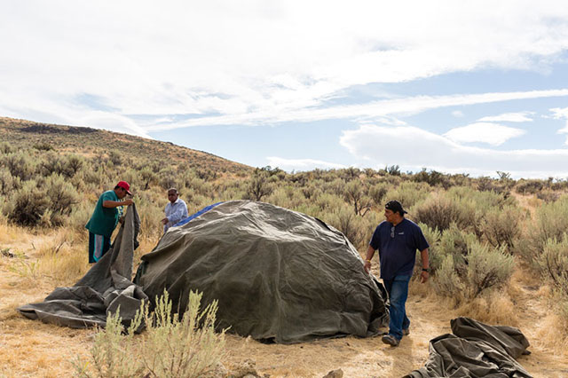 Murray Sope (left) and Joseph Holley (right) help Reginald Sope, a healer from the Shoshone-Paiute Tribe, place tarps over a ceremonial sweat-lodge frame in Tosawihi. (Photo: Joseph Zummo)