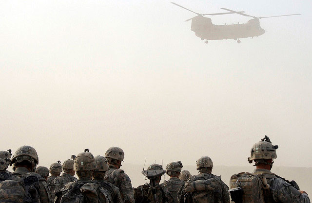US Army paratroopers watch as a CH-47 Chinook helicopter descends to pick them up for an air-assault mission July 17, 2009, during a dust storm at Forward Operating Base Kushamond, Afghanistan. Many careers, reputations and programs tied to the war industry depend upon the continuation of the failed Afghan war.