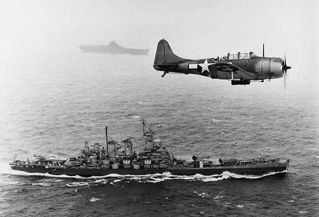 A US Navy Douglas SBD-5 Dauntless flies an antisubmarine patrol low over the battleship USS Washington en route to the invasion of the Gilbert Islands, November 12, 1943. World War II marked the beginning of the United States's transformation into the world's policing power, represented by ongoing overt and clandestine warfare.