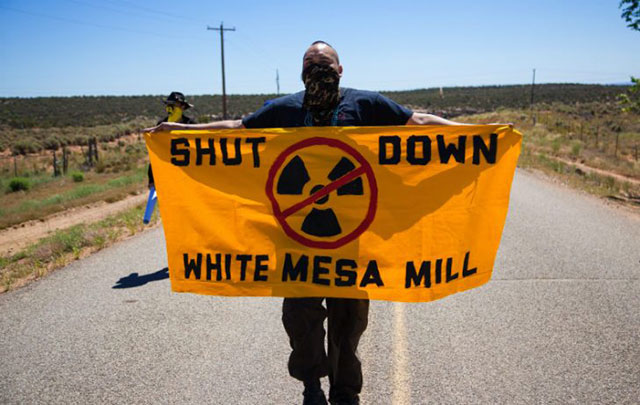 Bobby Mason, representative of Haul No!, carries a Shut Down White Mesa Mill sign through the gates of the mill. (Photo: Garet Bleir)