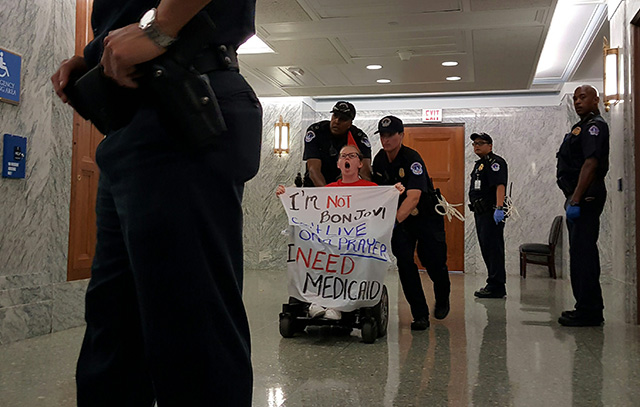 A protester in a wheelchair is arrested carrying a sign that reads: 